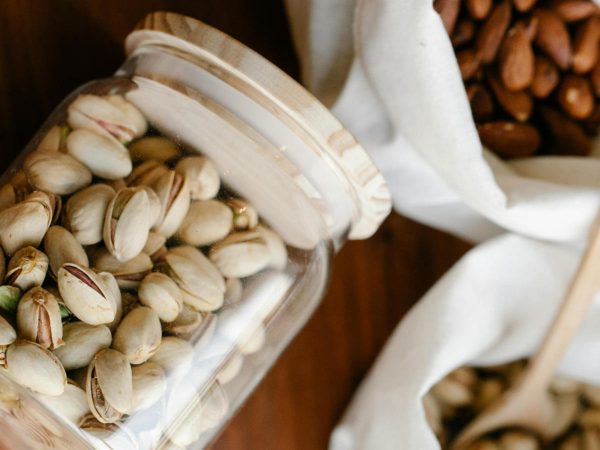 pistacchi in guscio dentro un barattolo con tappo ermetico in legno, altri pistacchi in guscio dentro un sacchetto di tela con cucchiaio in legno e un altro sacchetto di tela pieno di mandorle sgusciate